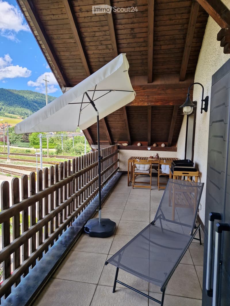 Balcony with wooden railing, umbrella, sun lounger, small table and chairs, and decorative items on the wall.