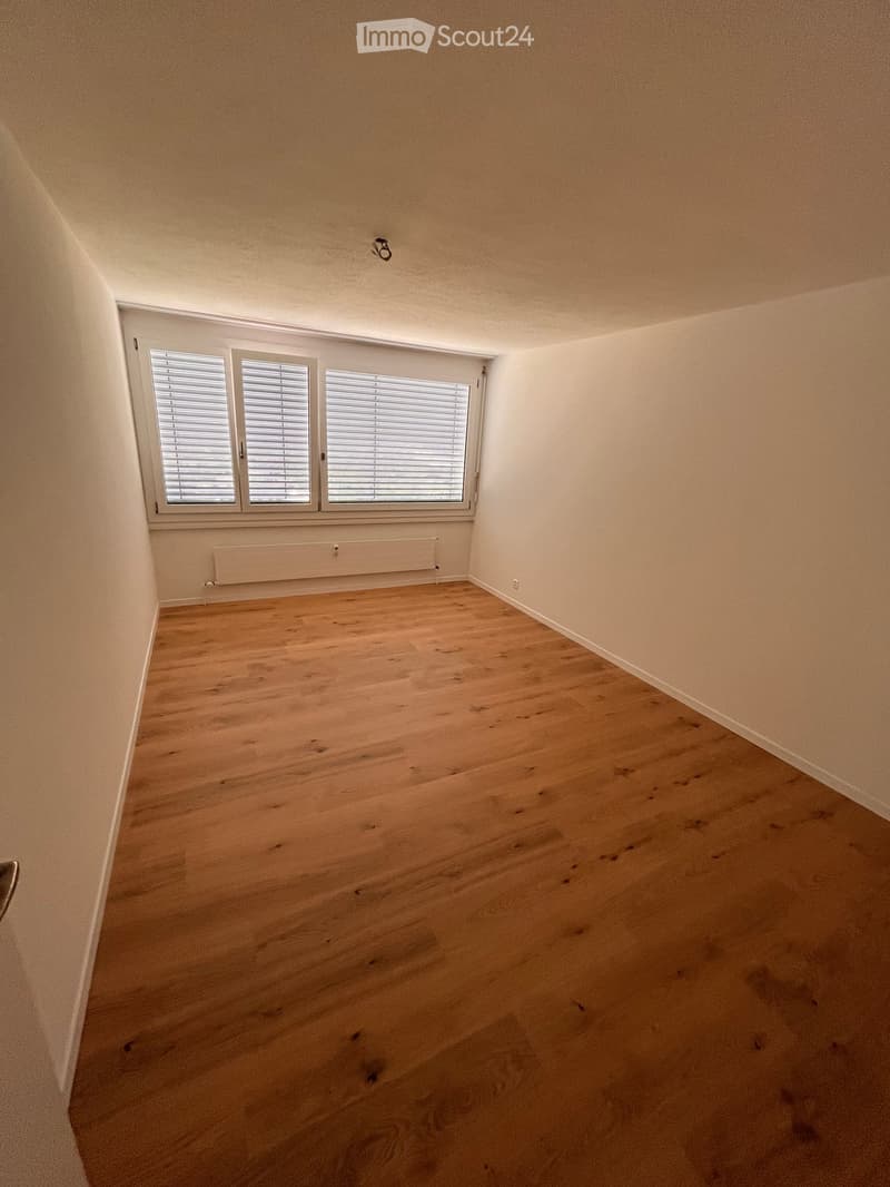Empty room with wooden flooring, white walls, and large windows with blinds. No furniture or equipment is present.