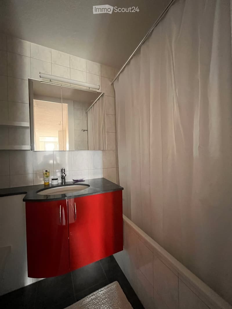 Modern bathroom with red cabinetry, black countertop, sink, mirror, and small items on the counter.