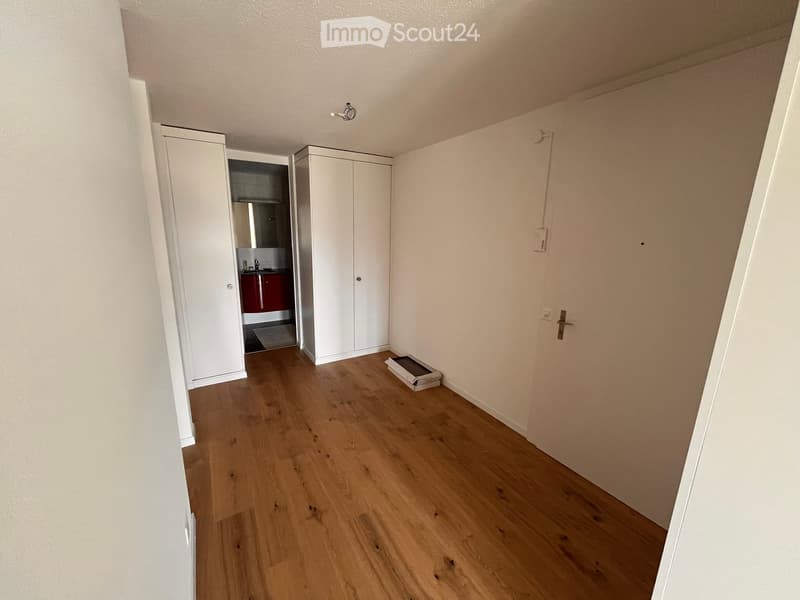 Empty room with wooden flooring, white walls, and built-in white wardrobes. A small adjacent bathroom is visible through an open door.