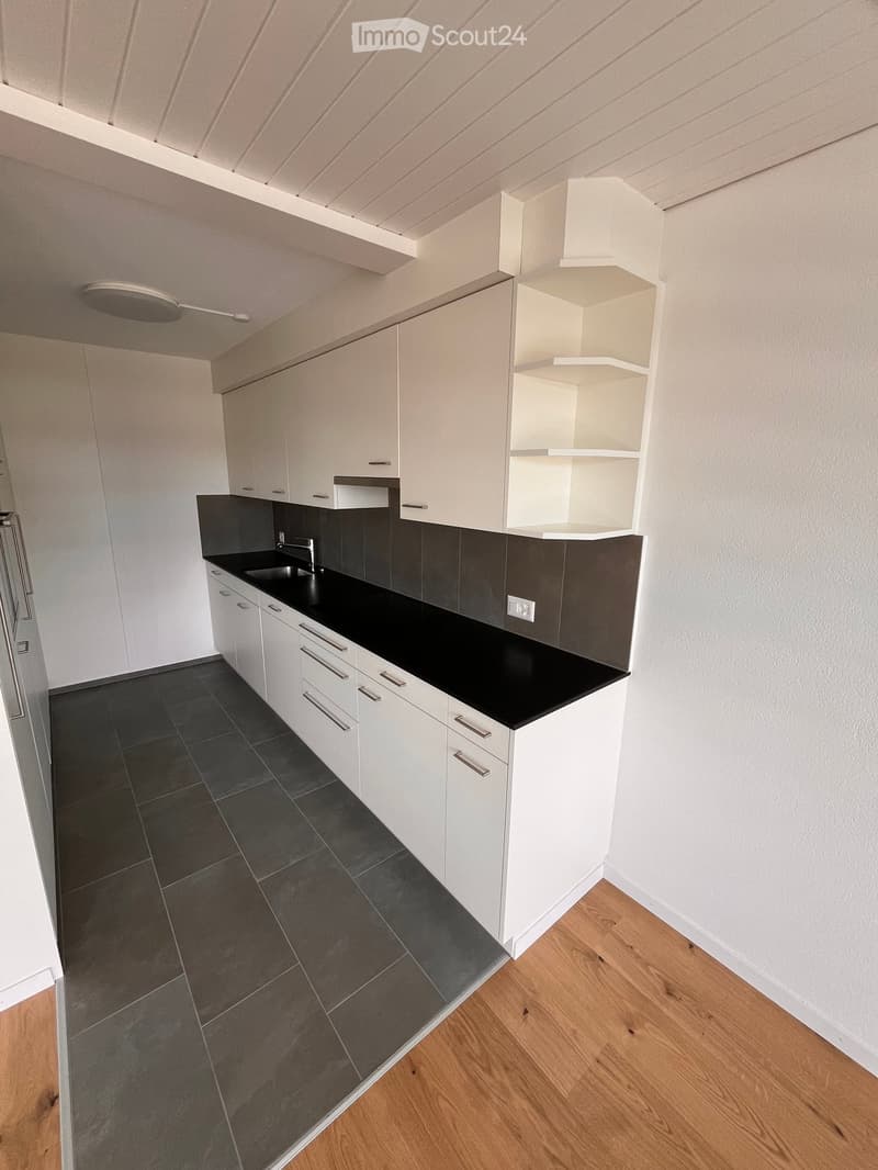 Modern kitchen with white cabinets, black countertops, and dark tiled flooring.