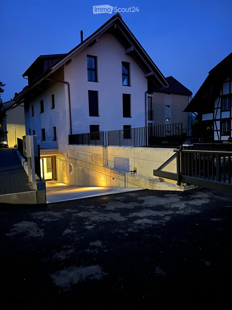Two-story house with a raised ground floor, illuminated entrance, and modern design.
