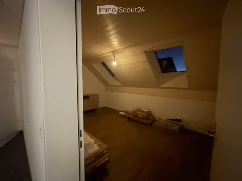 Empty attic room with wooden floor, white walls, skylight windows, and a small storage cabinet. No furniture or personal items present.