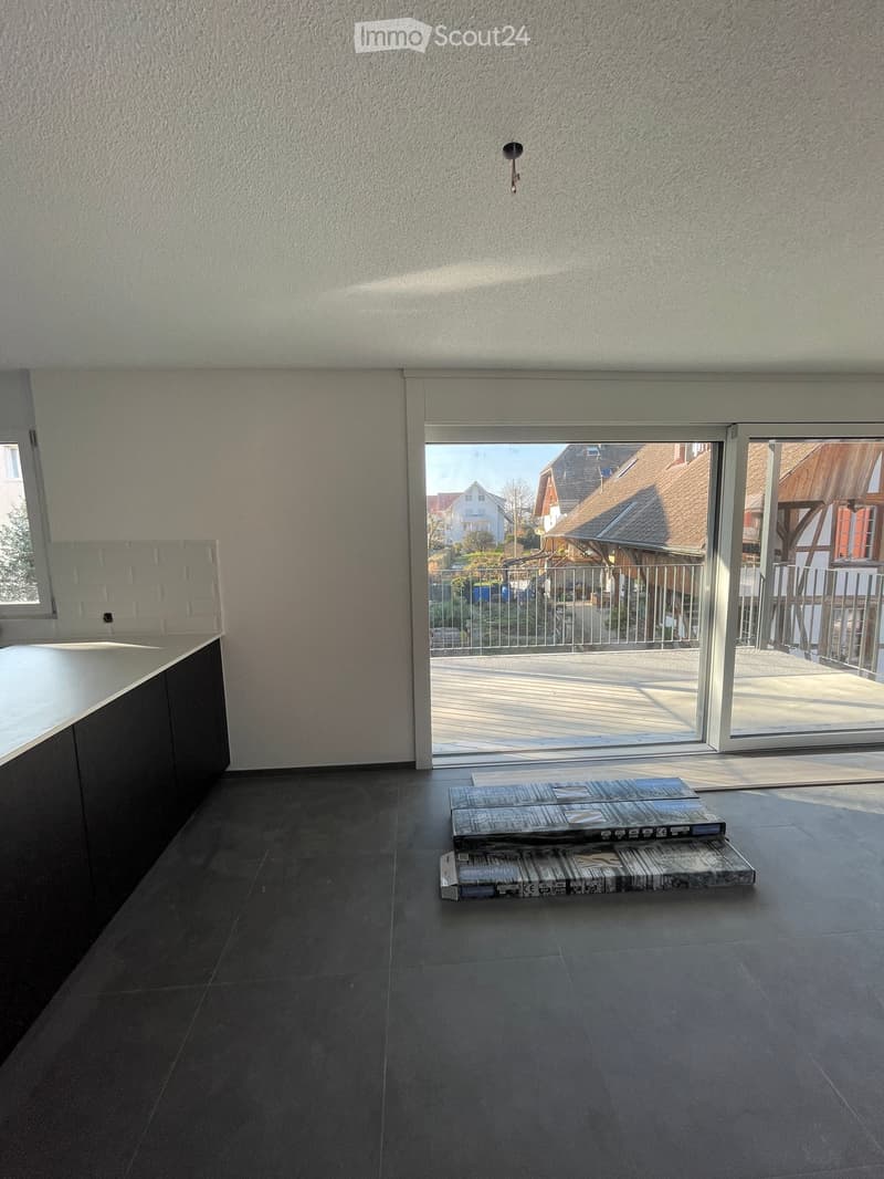 Empty room with dark tiled floor, white walls, and a large sliding glass door leading to a balcony with outdoor furniture visible.