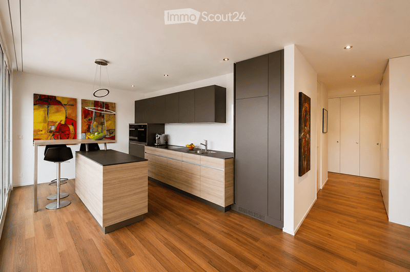 Modern kitchen with wooden island, black stools, sleek cabinets, stainless steel appliances, and framed artwork on walls.