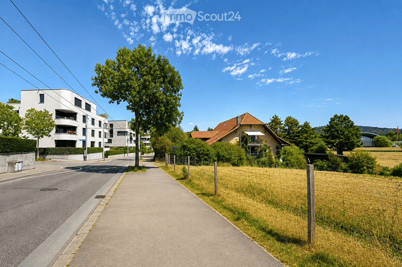 Residential street lined with modern apartment buildings and traditional houses, surrounded by greenery and trees.