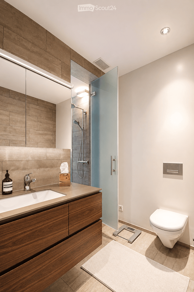 Modern bathroom with wooden cabinetry, a large mirror, a glass-enclosed shower, a toilet, and a sink with a modern faucet.