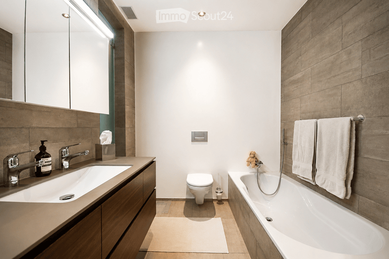 Modern bathroom with a double sink, bathtub, toilet, and large mirror. Wooden accents and white tiles.