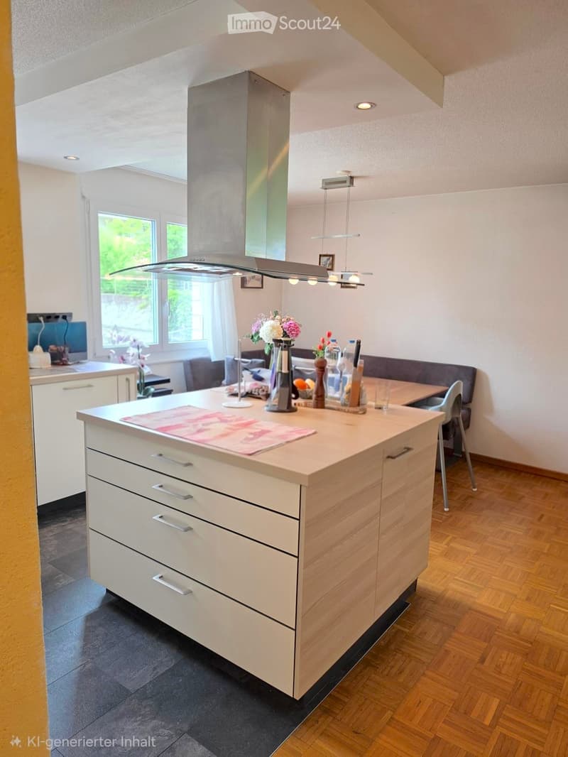 Modern kitchen with a central island, white cabinets, and wooden flooring. Features include a sink, a chair, a flower vase, and a light fixture.