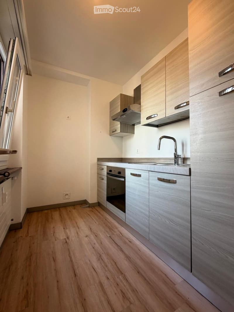 Modern kitchen with light wooden flooring, white walls, and grey cabinets. Features a sink with a modern faucet, an oven, and overhead storage cabinets.