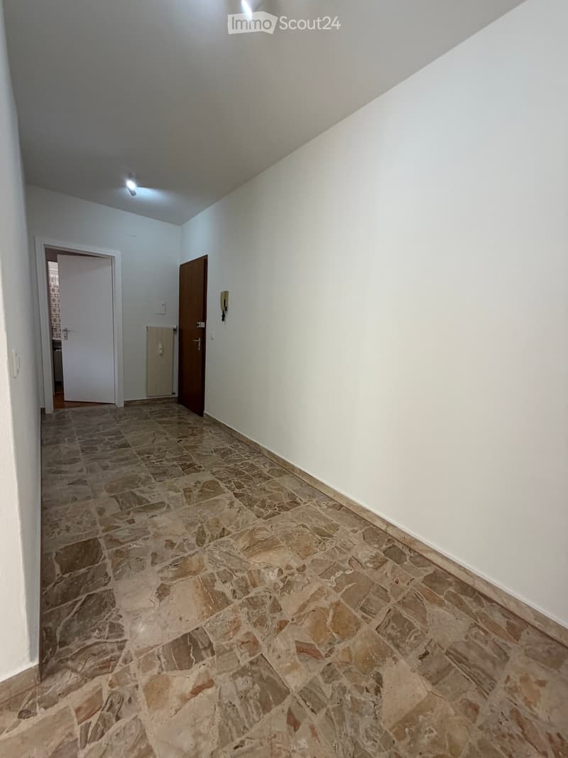 Empty hallway with stone tiled floor, white walls, and two doors, one leading to another room.