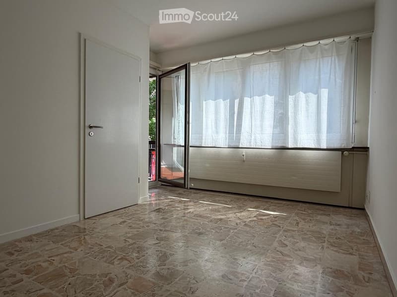 Empty hallway with tiled floor, white walls, a closed door on the left, and an open sliding door leading to a balcony with white curtains.