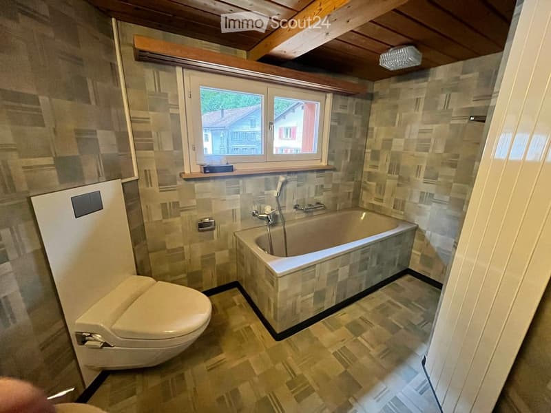 Bathroom with a toilet, bathtub, and window overlooking a house exterior.