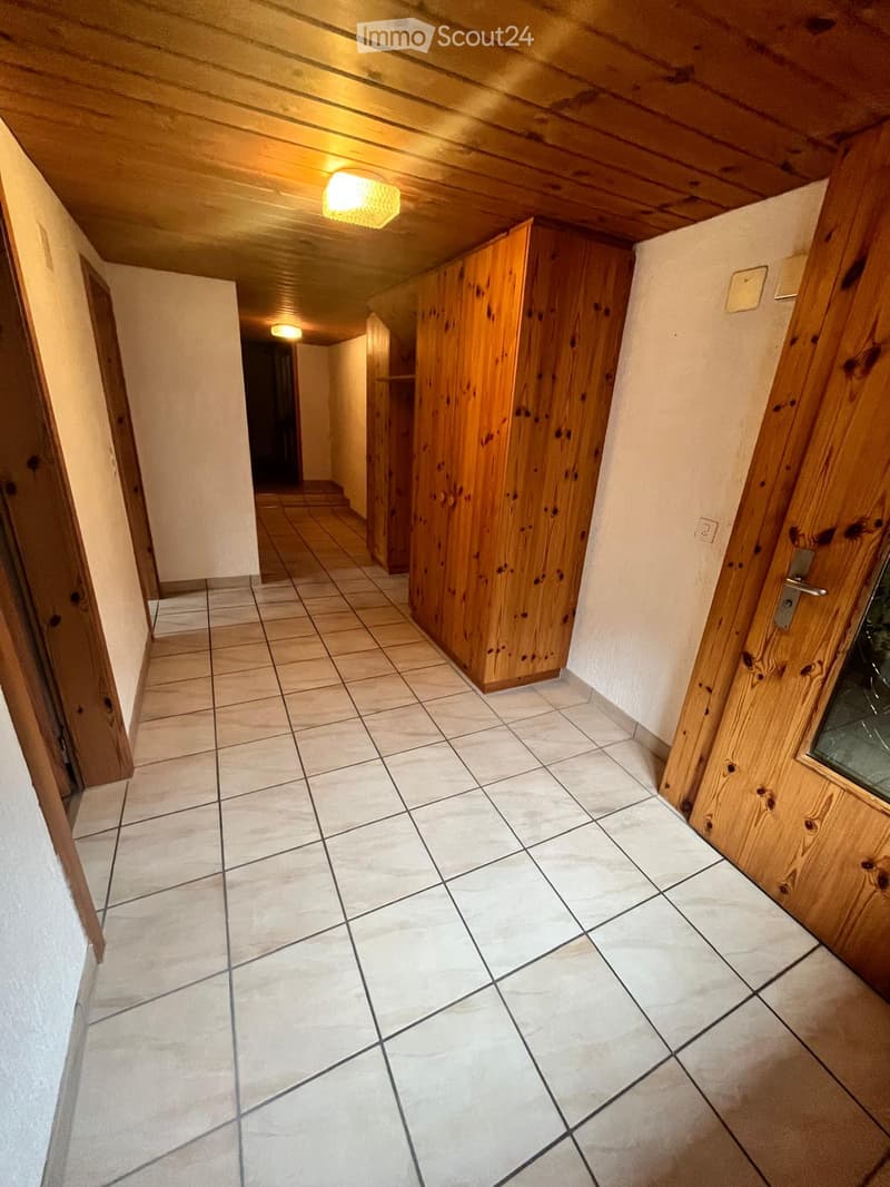 A narrow hallway with tiled flooring, wooden doors, and built-in wooden cabinets on one side. The ceiling has exposed wooden beams and recessed lighting.
