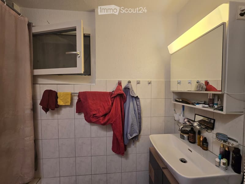 Bathroom with tiled walls, a white sink, a mirror with built-in lighting, and a towel rack with several towels.