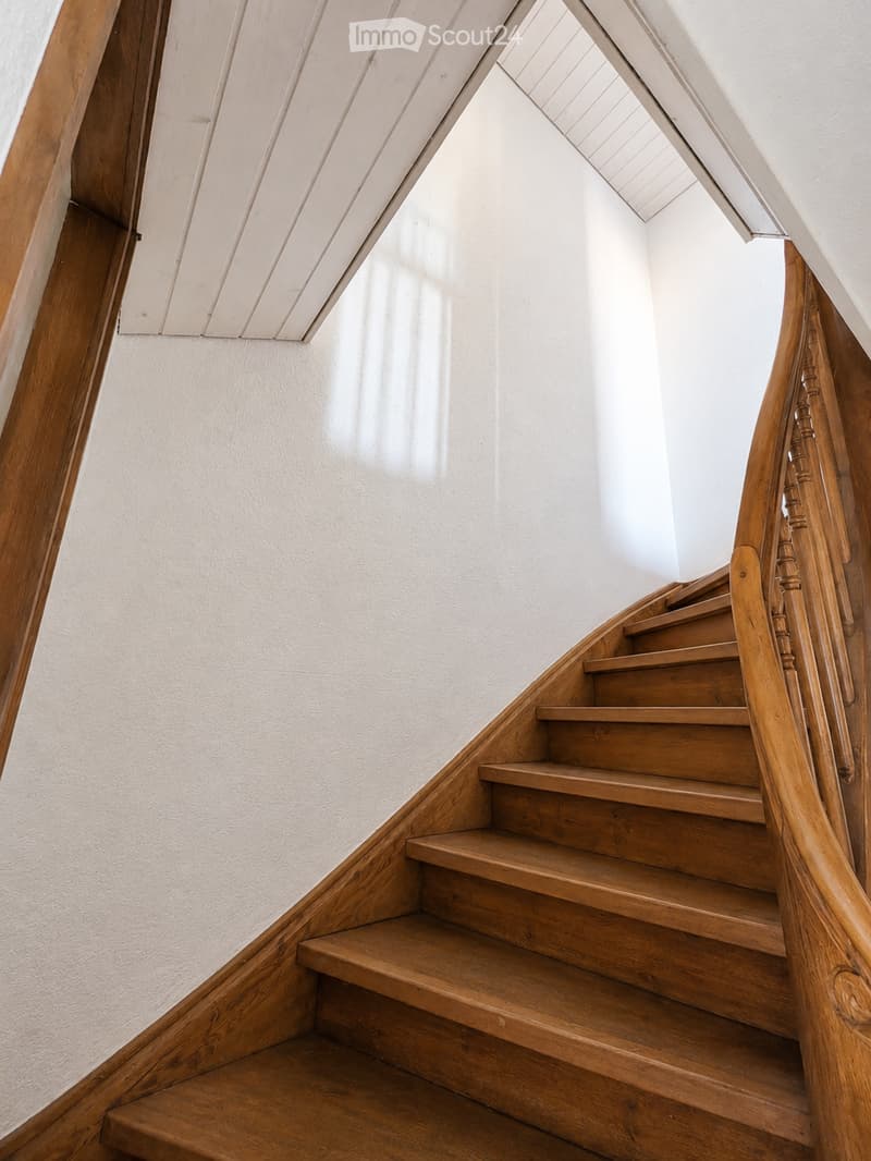 Wooden staircase with a curved handrail and light-colored walls.