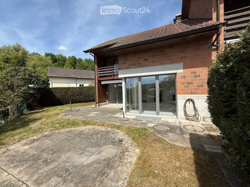 Two-story brick house with a balcony, large glass doors, and a paved patio area.