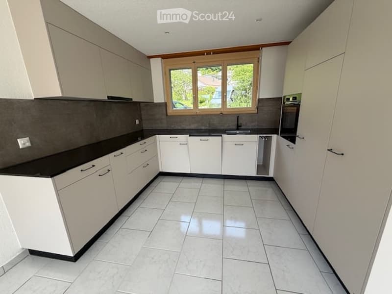 Modern kitchen with white cabinets, black countertops, and a large window overlooking a garden. Features include a sink, oven, and tiled flooring.