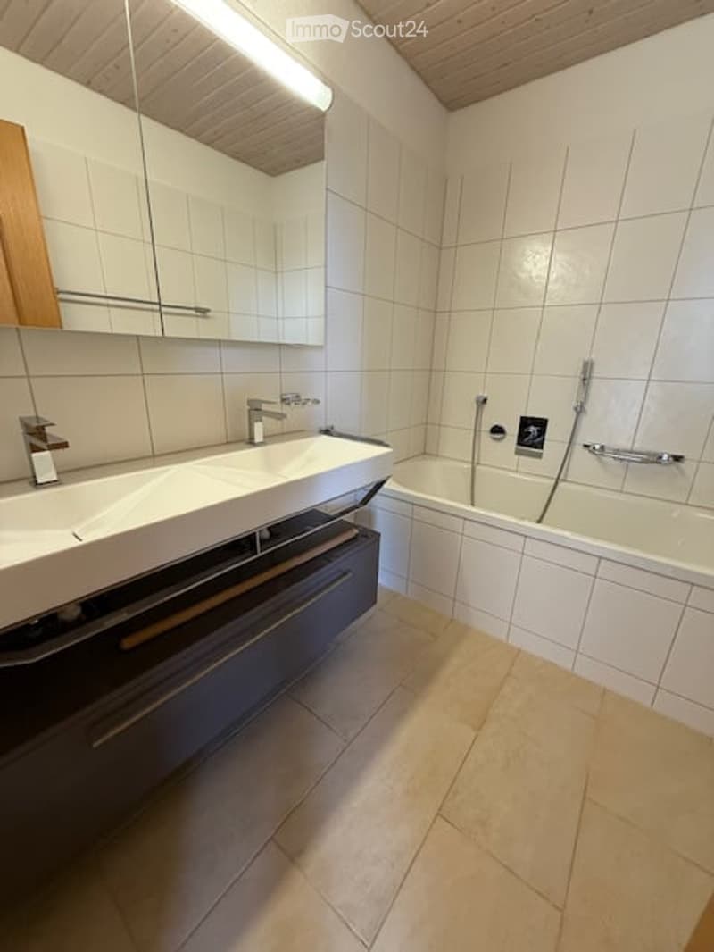 Modern bathroom with white tiles, a large sink, a bathtub, and a mirrored cabinet.