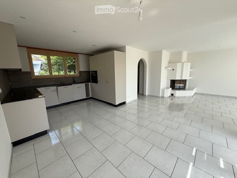 Open-plan kitchen and living area with white cabinetry, tiled floor, and a built-in fireplace. The space is completely empty with no furniture or appliances.