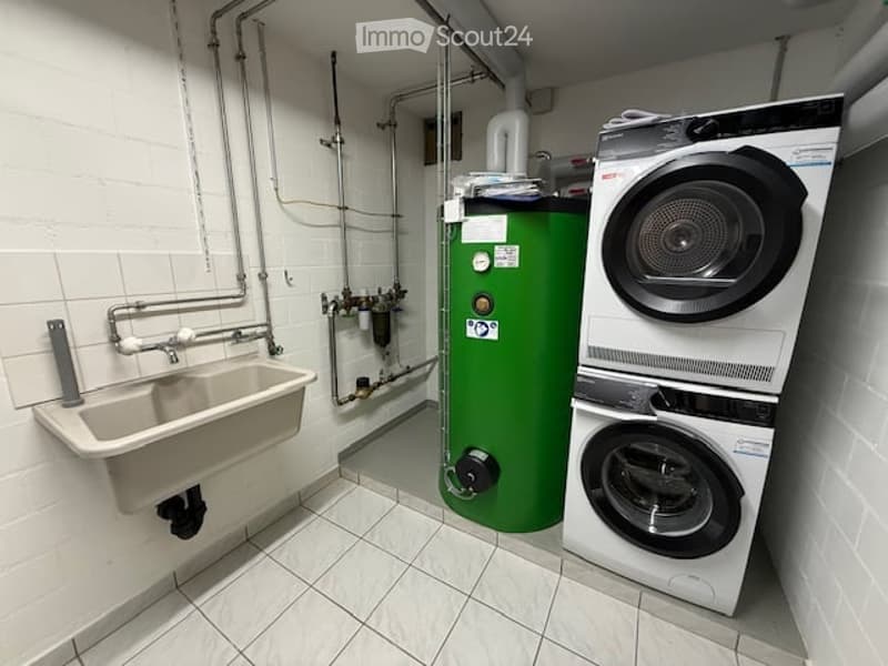 Utility room with a sink, stacked washing machine and dryer, and a green water heater. White tiled walls and floor.