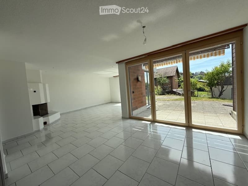 Bright, unfurnished living space with large sliding glass doors leading to an outdoor area, tiled floor, and a built-in fireplace on the left side.