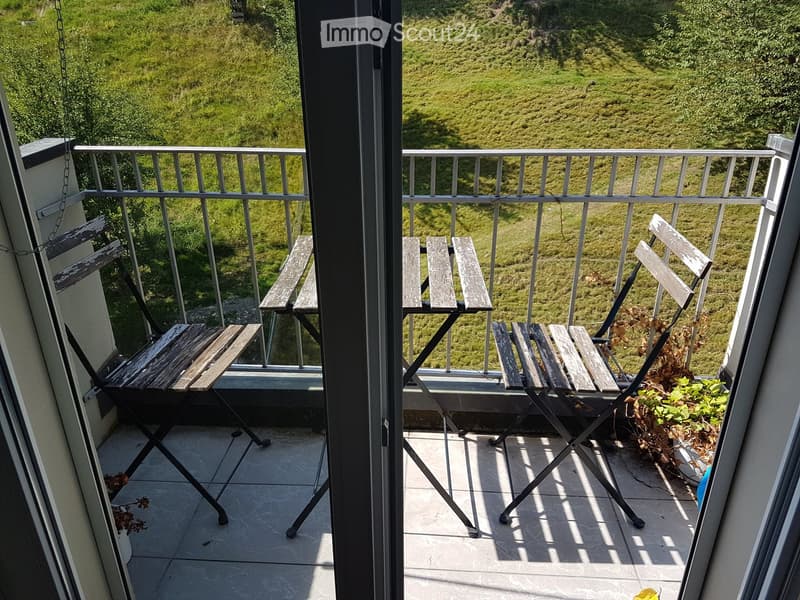 Balcony with tiled floor, metal railing, and several wooden folding chairs, overlooking a grassy hillside.