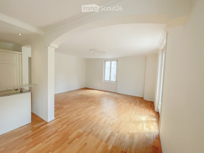 Empty room with light wooden flooring, white walls, and a small counter area on the left side.