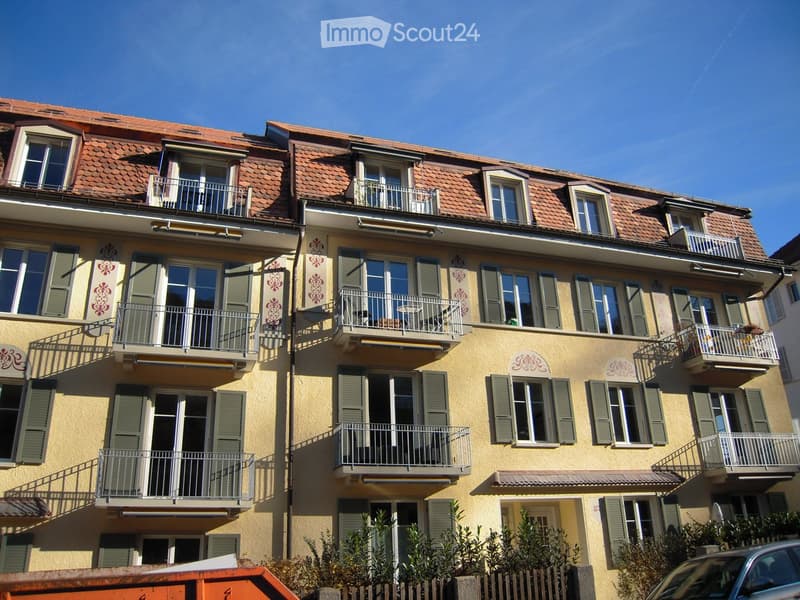 Multi-story residential building with yellow facade, green shutters, multiple balconies, and a red-tiled roof.