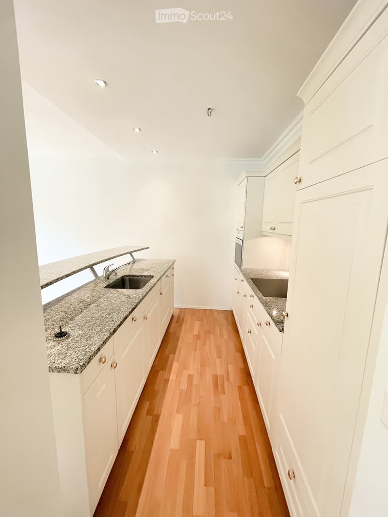Modern kitchen with white cabinets, granite countertops, wooden flooring, and built-in appliances including a sink and oven.