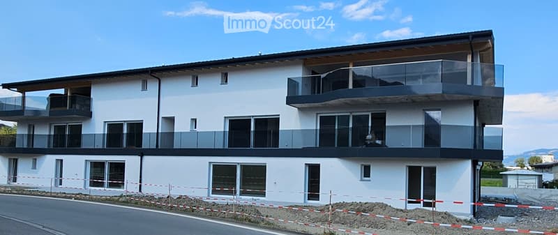 Modern two-story house with white facade, large windows, and multiple balconies with glass railings.