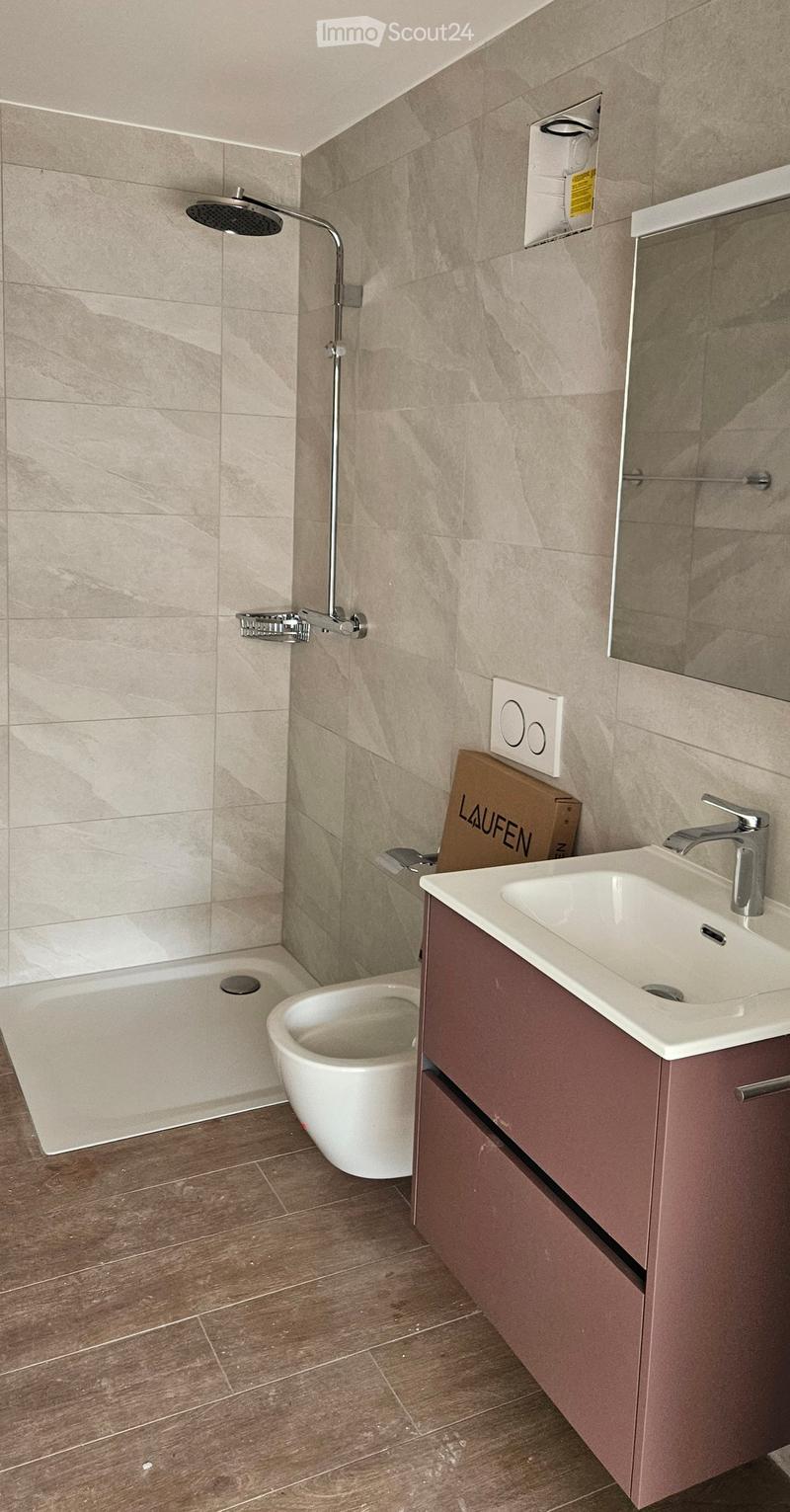 Modern bathroom with a sink, toilet, shower, and mirror. Features a wooden floor and beige tiled walls.
