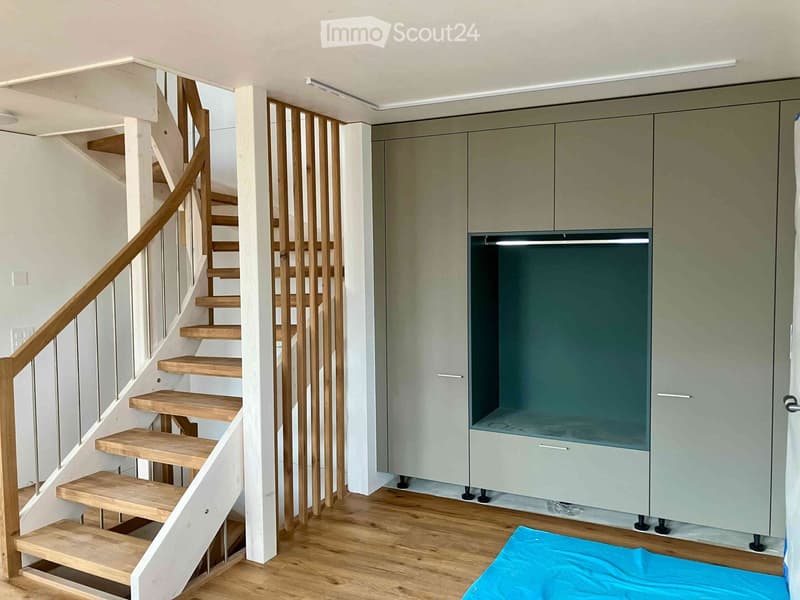 Modern staircase with wooden steps and a wooden handrail, adjacent to a grey cabinet with a mirrored front.