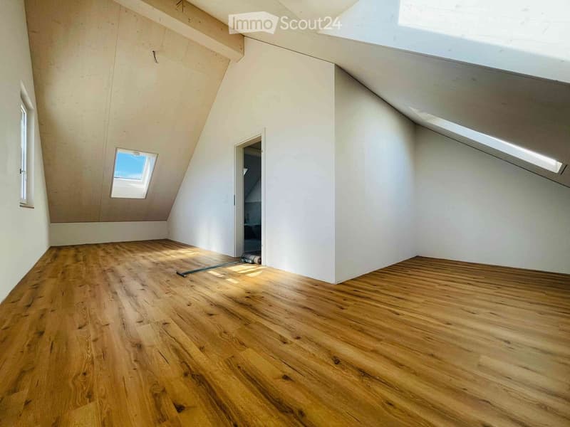 Empty attic room with wooden flooring, white walls, and skylight windows. No furniture or equipment present.