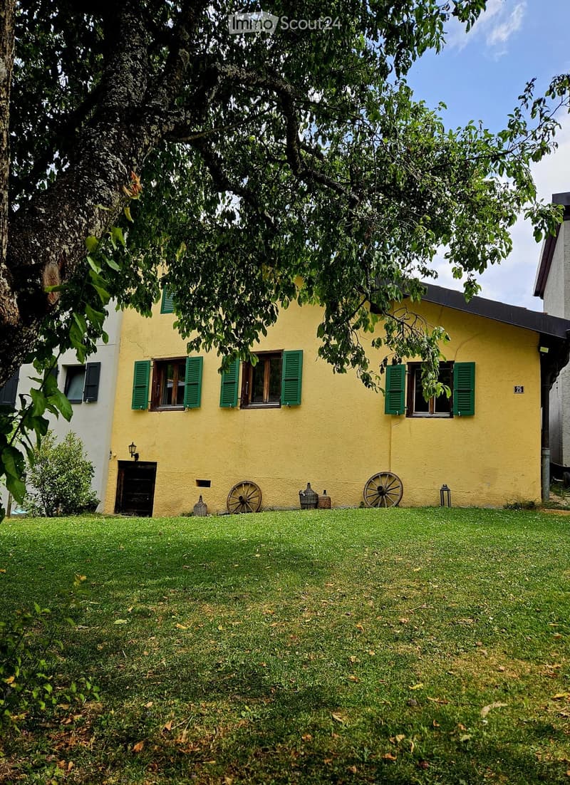 Yellow two-story house with green shutters, a well-maintained lawn, and decorative items like wheelbarrows and baskets near the entrance.