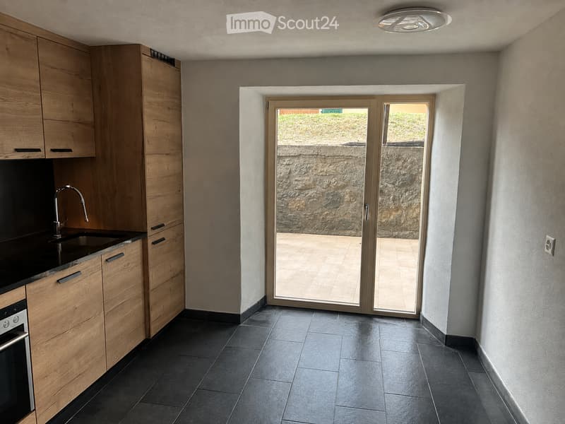 Modern kitchen with wooden cabinets, black countertop, sink, faucet, and built-in oven. Sliding glass door leads to a tiled outdoor area.