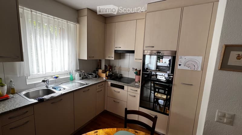 Modern kitchen with white cabinets, granite countertops, stainless steel appliances, and a small dining area with a wooden table and chair.