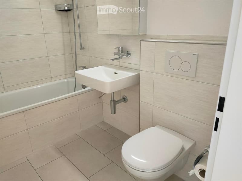 Modern bathroom with beige tiles, white toilet, sink, bathtub, and a mirror above the sink.