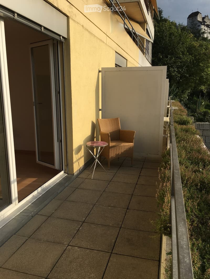 Balcony with tiled floor, a wicker chair, and a small round table, adjacent to a sliding glass door leading to an interior space.