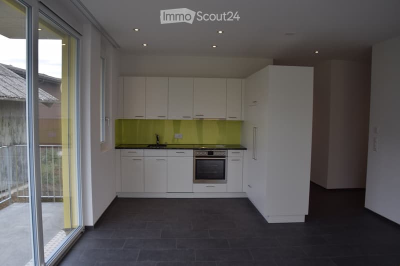 Modern kitchen with white cabinets, a sink, and an oven, featuring a green backsplash and dark tiled flooring.