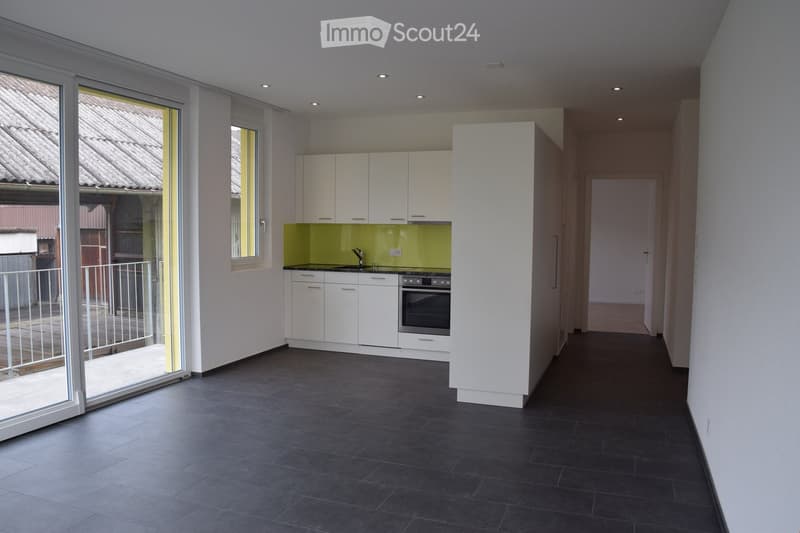 Modern kitchen with white cabinets, a green backsplash, and dark tiled flooring. Features a sink, faucet, and oven, with large windows and a balcony access.