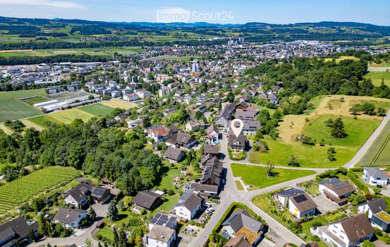 Aerial view of a suburban neighborhood with houses, green spaces, and surrounding countryside.
