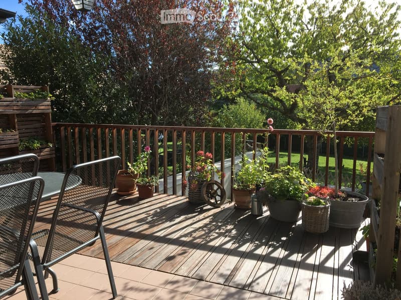 Wooden deck with railing, potted plants, and a metal chair.