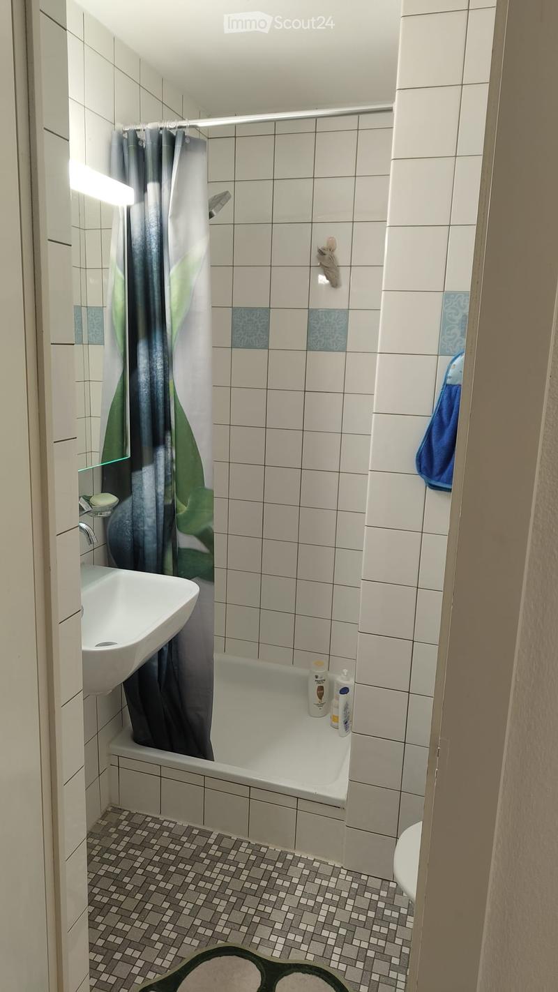 Bathroom with white tiled walls, a bathtub, a sink, a shower curtain, and a towel hanging on the wall.