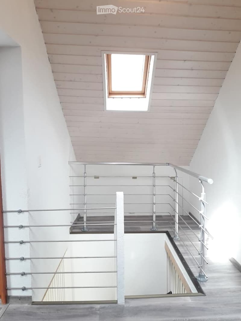 Modern interior staircase with wooden slatted ceiling, metal railing, and a skylight window above.
