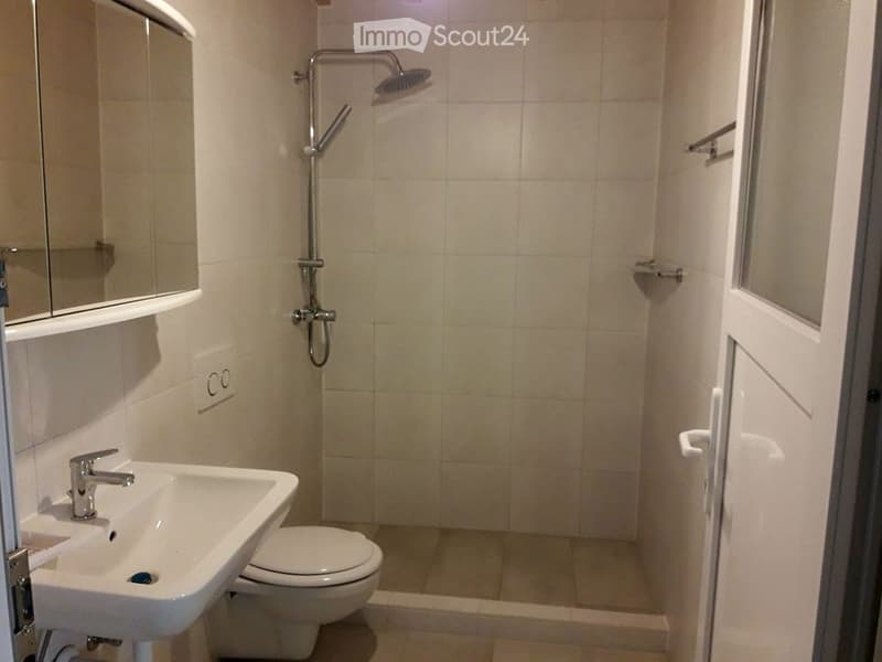 Modern bathroom with a white sink, toilet, shower, and mirror. The walls are tiled in light beige, and the floor is also tiled.