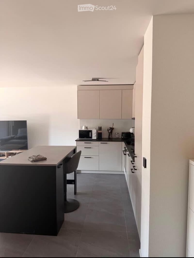 Modern kitchen with white cabinets, a black island, and various appliances including a microwave and oven. The space features a grey tiled floor and a sleek, contemporary design.