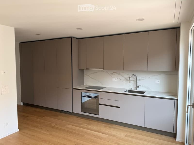 Modern kitchen with grey cabinets, marble backsplash, and wooden flooring.