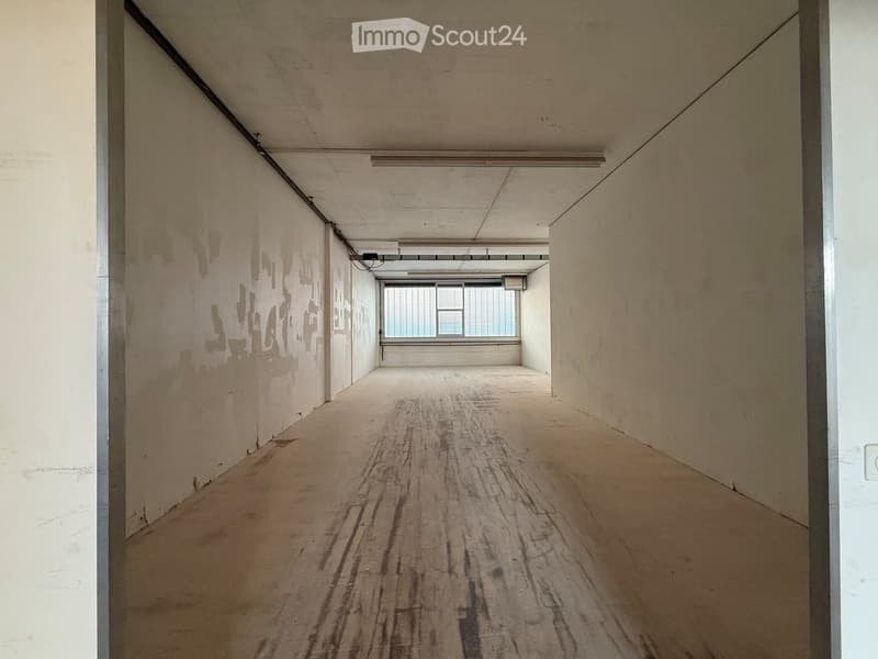 Empty hallway with wooden flooring, white walls, and a single window at the end.