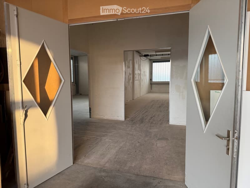 Empty room with bare walls, concrete floor, and open doors leading to other rooms.